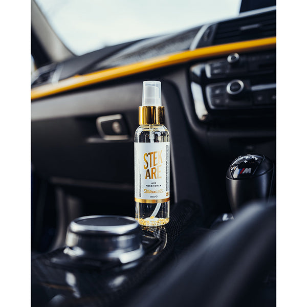 A spray bottle of Stjarnagloss Stekare on the center console of a black car.
