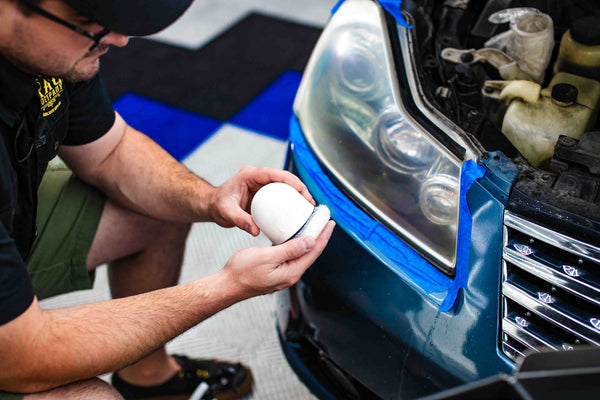 A person holding the white hand block with a blue car in the background.