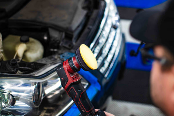 The Koch Chemie headlight polish pad with a car in the background.