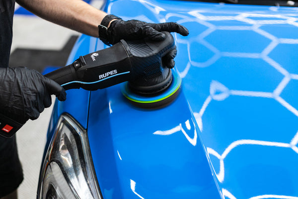 A person using the Koch Chemie Polish and Sealing pad on a blue car.