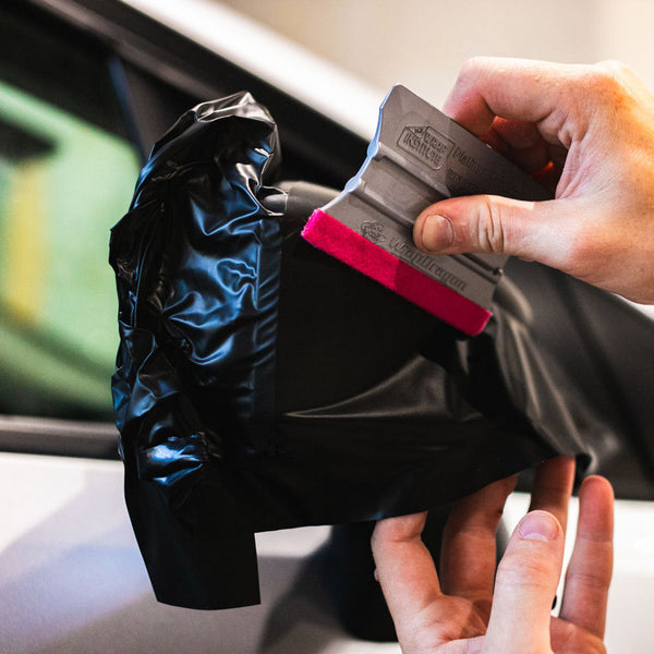 A person using the Yellotools Squeegee to lay vinyl on a car's side mirror.