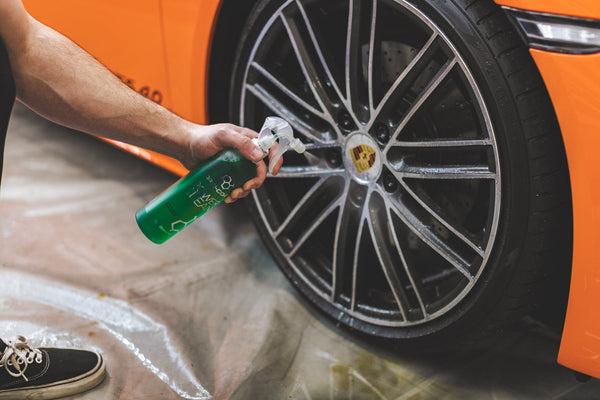 A closeup of a person spraying an orange Porches' tire with Opti-Coat Power Clean.