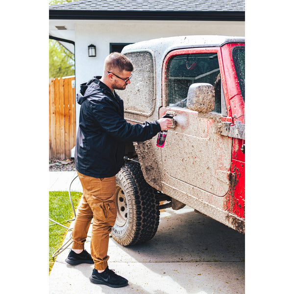 A person spraying off a red jeep covered in mud with a hose.