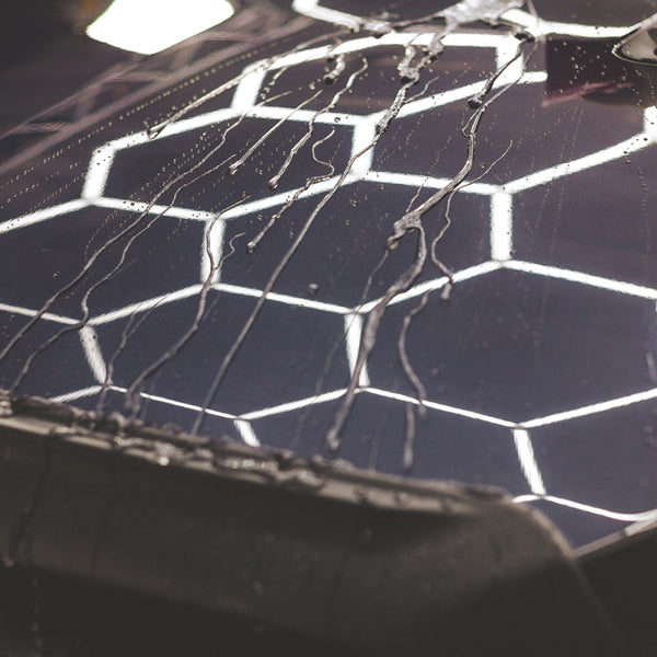 Streams of water flowing down the hood of a black car.