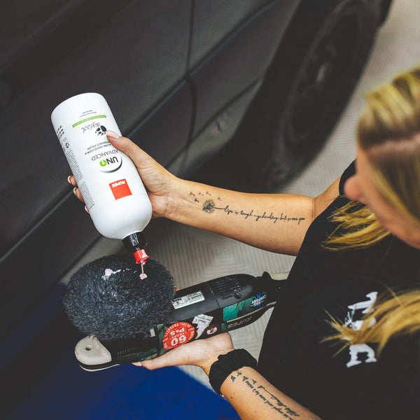 A closeup of a person pouring Rupes Uno Advanced onto a polisher in front of a black car.