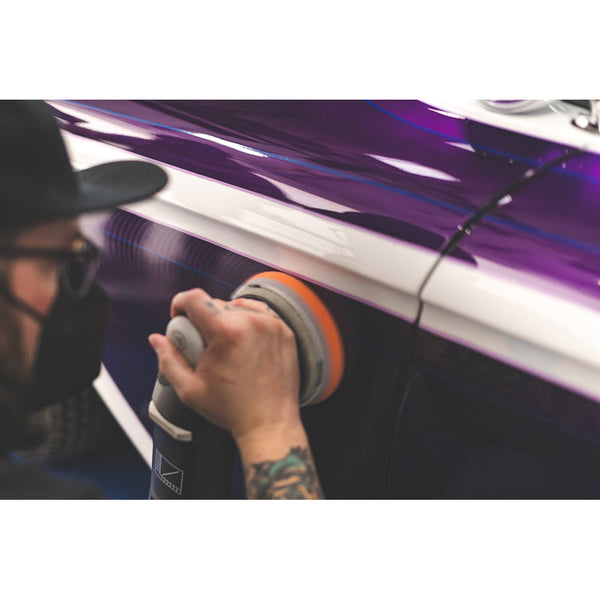 A closeup of a person polishing a purple car.
