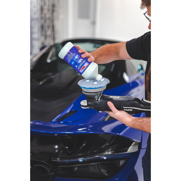 A Person pouring polisher onto a polishing pad in front of a blue sports car.