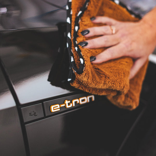 A person scrubbing a black car with a brown Wolfpack towel.