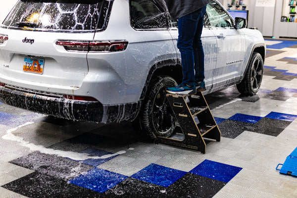 A person using a three step Wrap Step to clean the top of their white Jeep Cherokee.