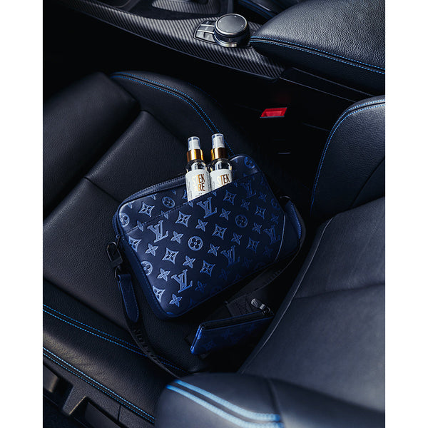 A black Luis Vuitton bag with two bottles of  Stjarnagloss Stekare in it. The bag is laying on a car's black leather seat.