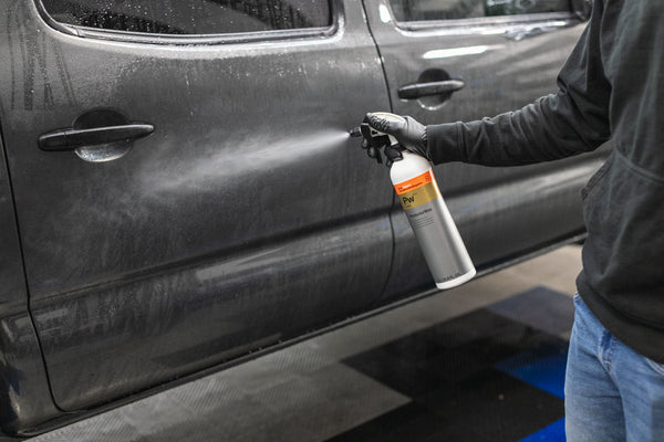 A person spraying Koch Chemie Protector Wax onto a grey Toyota Tacoma .