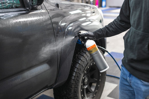 A person spraying Koch Chemie Protector Wax onto a grey Toyota Tacoma .